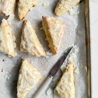 Freshly baked lemon white chocolate scones on baking sheet with a knife.