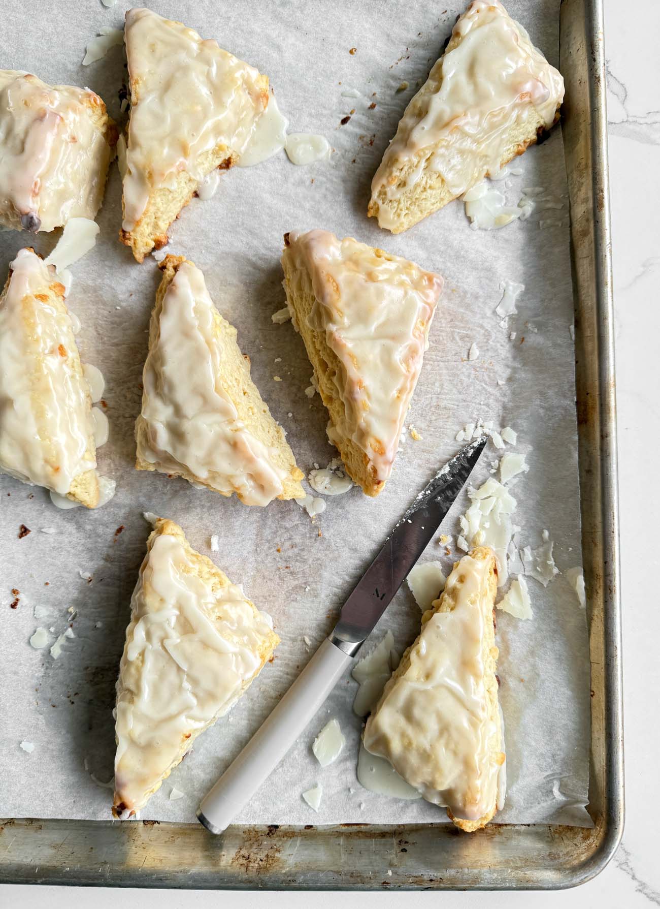 Freshly baked lemon white chocolate scones on baking sheet with a knife.