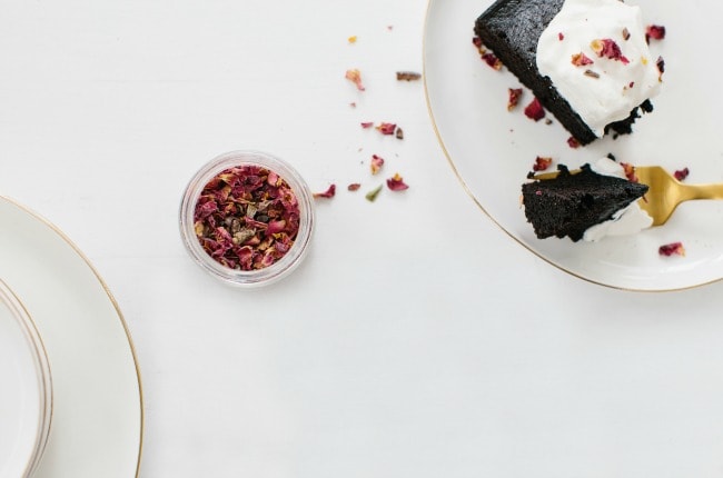 A slice of chocolate olive oil cake next to a jar of dried rose petals
