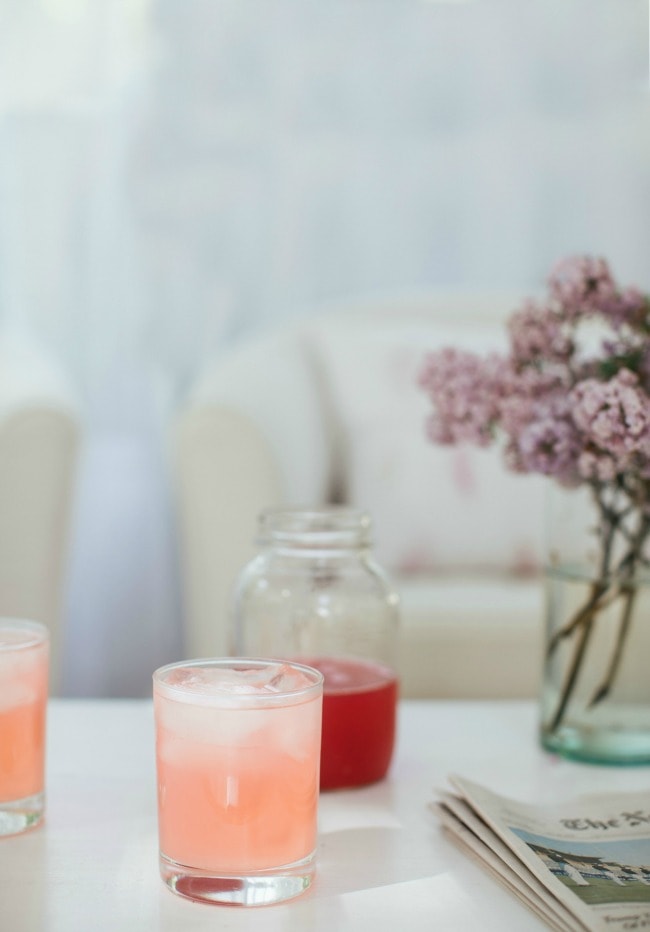 Glasses of rhubarb lemonade on a table next to lilacs. | The Vanilla Bean Blog