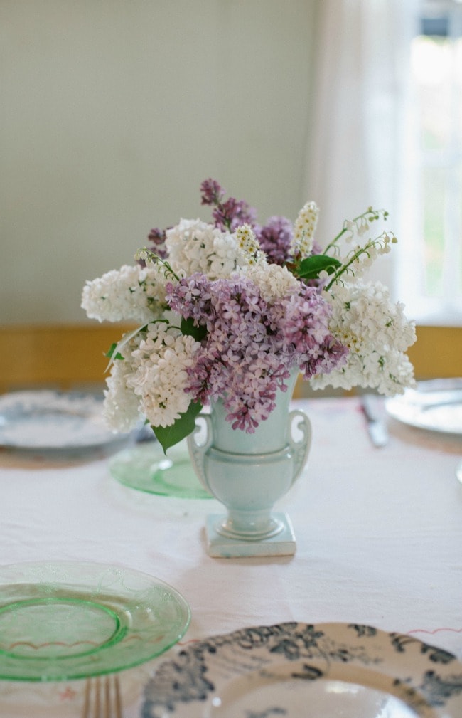 A bouquet of white and purple lilacs on a table set for a meal.