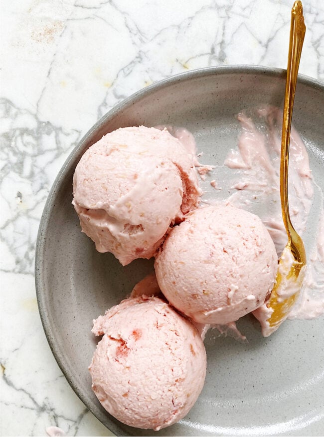 strawberry rhubarb ice cream in a dish with gold spoon