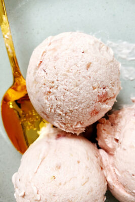 strawberry rhubarb ice cream in dish with gold spoon