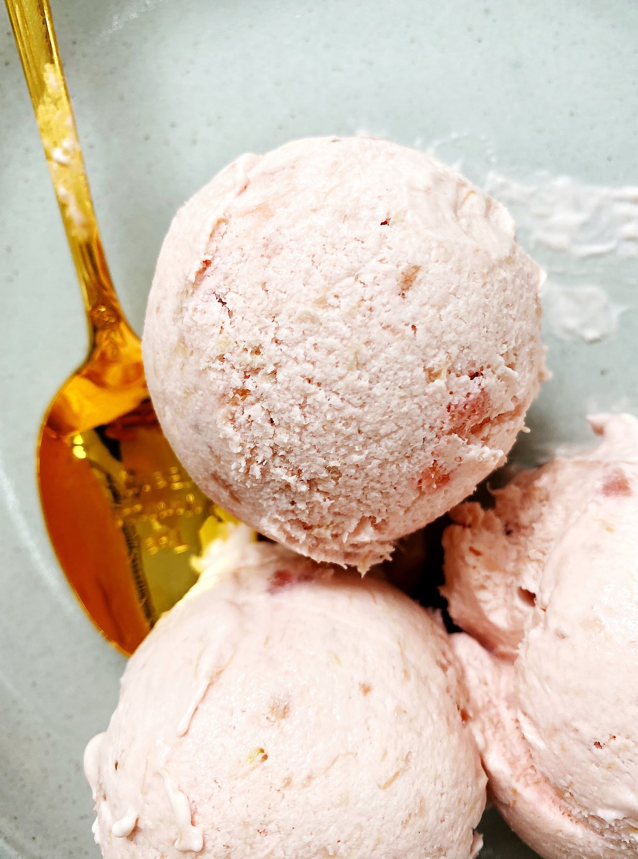 strawberry rhubarb ice cream in dish with gold spoon