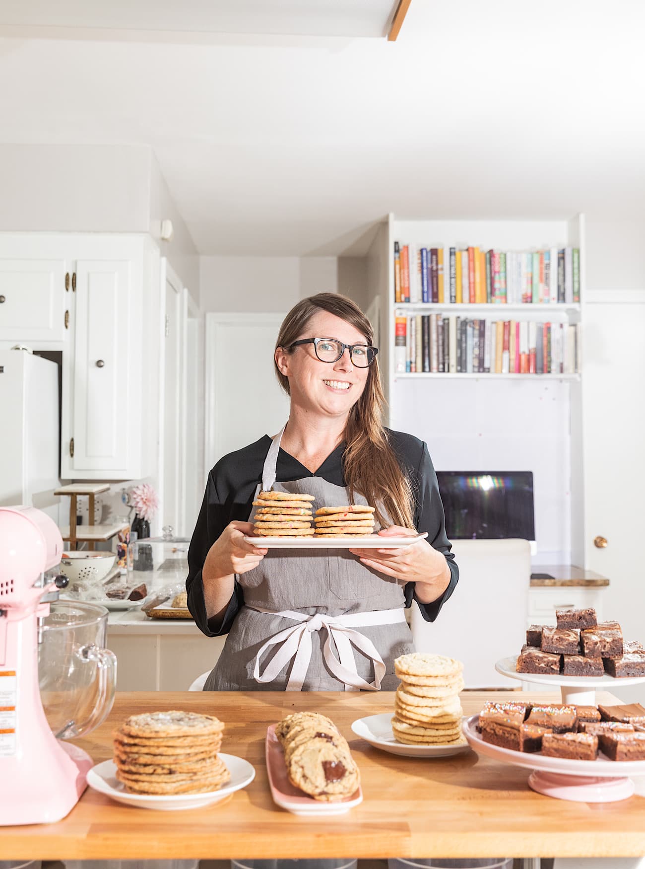 Sarah Kieffer wearing a grey apron holding a plate of stacked cookies