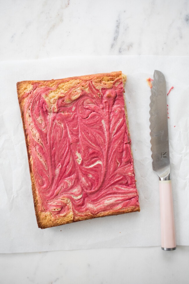 raspberry white chocolate brownies on white parchment paper with pink knife to the right