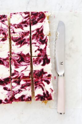 no-bake cheesecakes bars with cranberries, sitting next to a pink knife