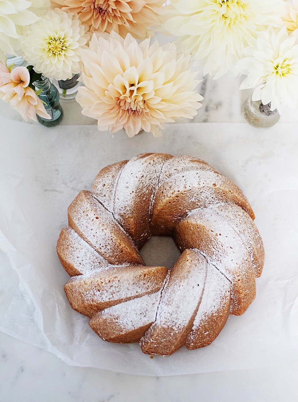 vanilla bundt cake with vases of dahlias surrounding it. 