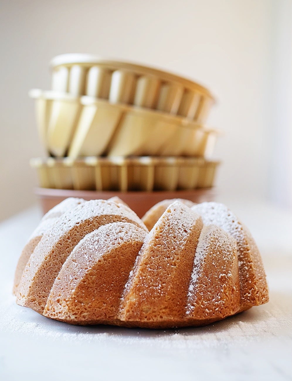 vanilla bundt cake with bundt cake pans stacked behind it