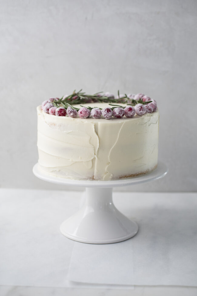 white chocolate cake with sugared cranberries on marble cake stand