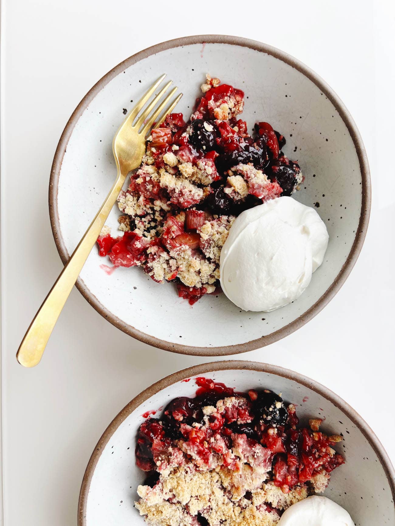 cherry rhubarb crisp in a bowl with whipped cream and gold fork