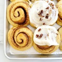 carrot cake cinnamon rolls frosted on a sheet pan