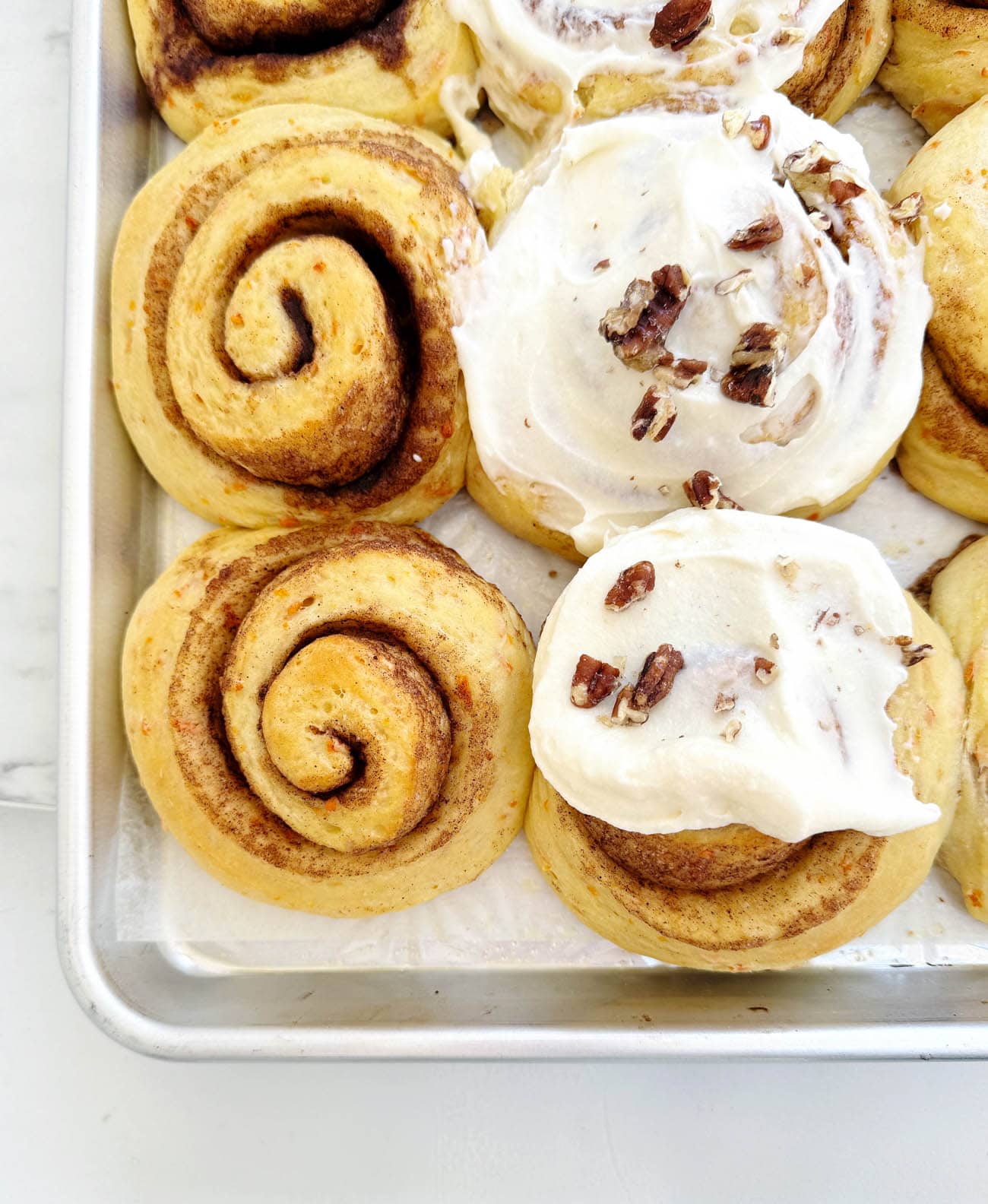 carrot cake cinnamon rolls frosted on a sheet pan
