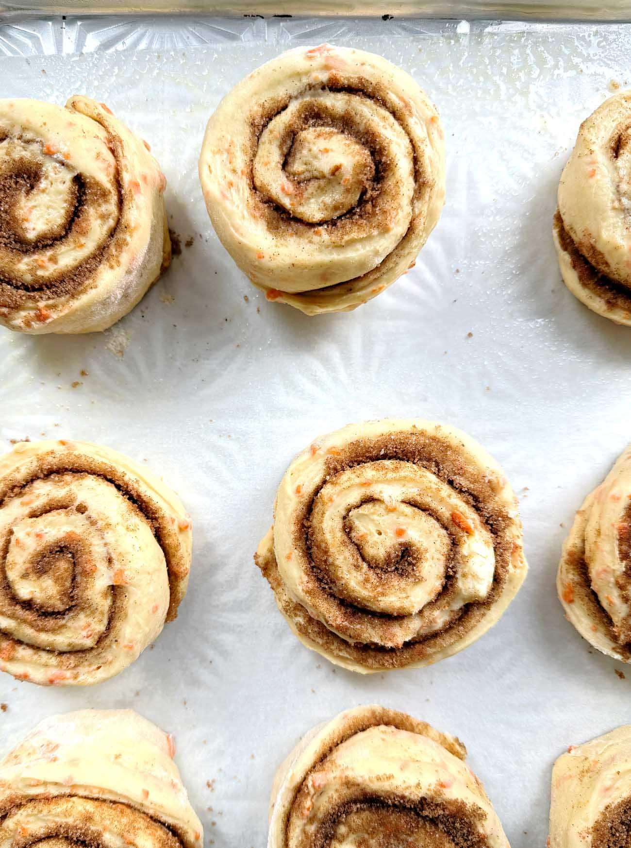 carrot cake cinnamon rolls before being baked, on a sheet pan