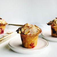 Delicious cherry almond muffin topped with sliced almonds on a white plate.