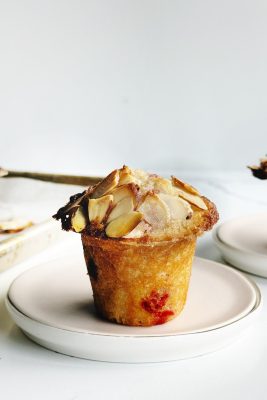 Delicious cherry almond muffin topped with sliced almonds on a white plate.