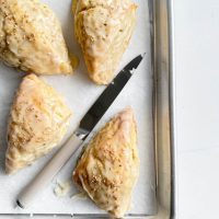 Fresh banana bread scones drizzled with toasted sesame icing on baking sheet.