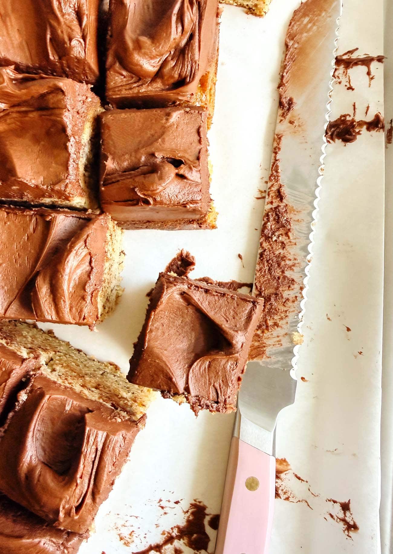 Close-up of banana bread bars topped with fudge buttercream and a serrated knife.